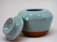 Load image into Gallery viewer, Turquoise jar with a lid leaning against iton a white background.