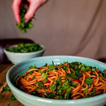 Load image into Gallery viewer, Turquoise pasta bowl with spaghetti sprinkled with pasta.  Hand in the background holding parsley.
