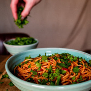 Turquoise pasta bowl with spaghetti sprinkled with pasta.  Hand in the background holding parsley.