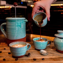 Load image into Gallery viewer, Turquoise cafetiere with 2 espresso cups and coffee being poured from a turquoise mini jug.
