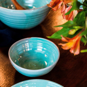 Small turquoise bowl with a large bowl in the background sitting on a dark wooden table.