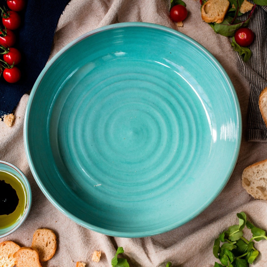 Wide shallow turquoise Bowl seen from above with tomatoes rocket and bread around it.
